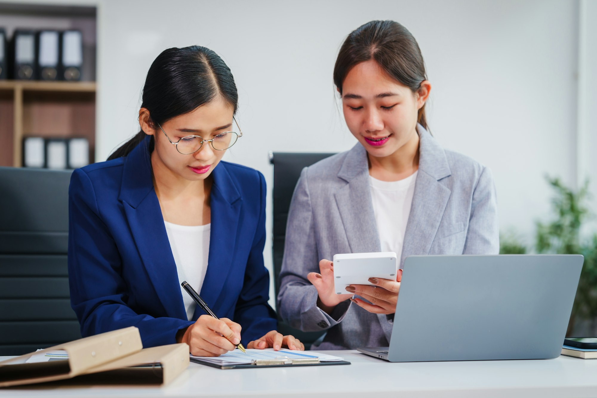 Two Asian businesswomen collaborate on stock market strategies and financial services, exchanging
