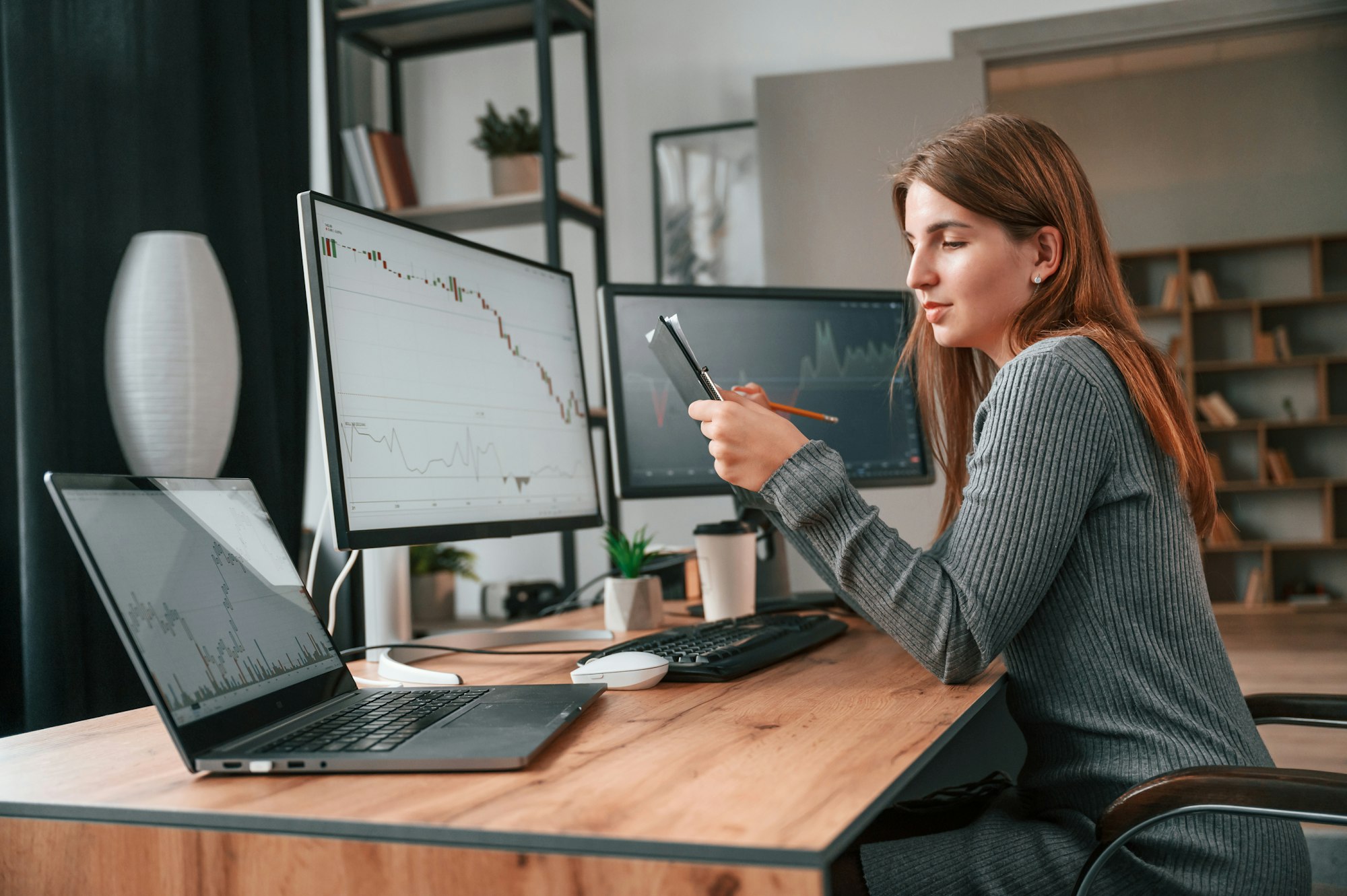 Young woman is sitting by computer and monitoring stock exchange